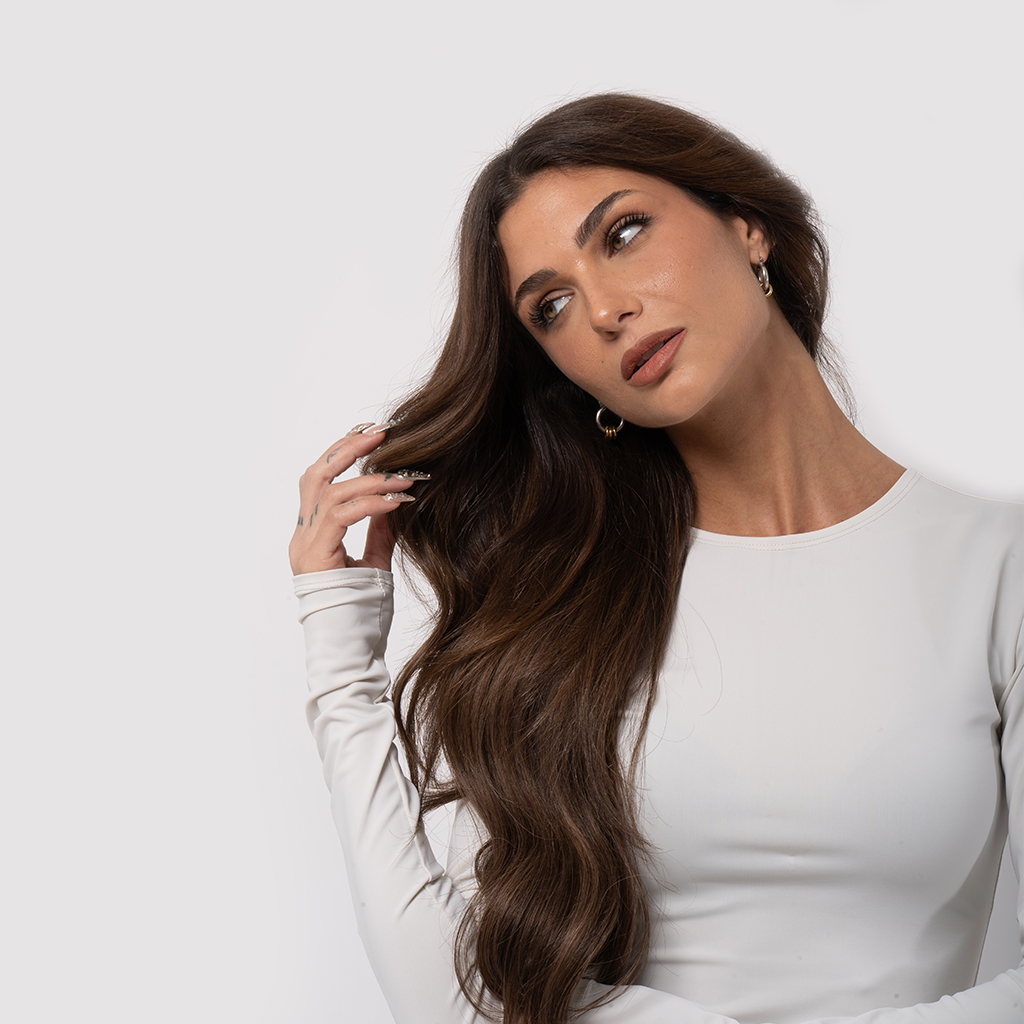 Brunett woman with Hair Extension installed by Emilly Hadrill Salon holding her hair and contemplating about hair care.