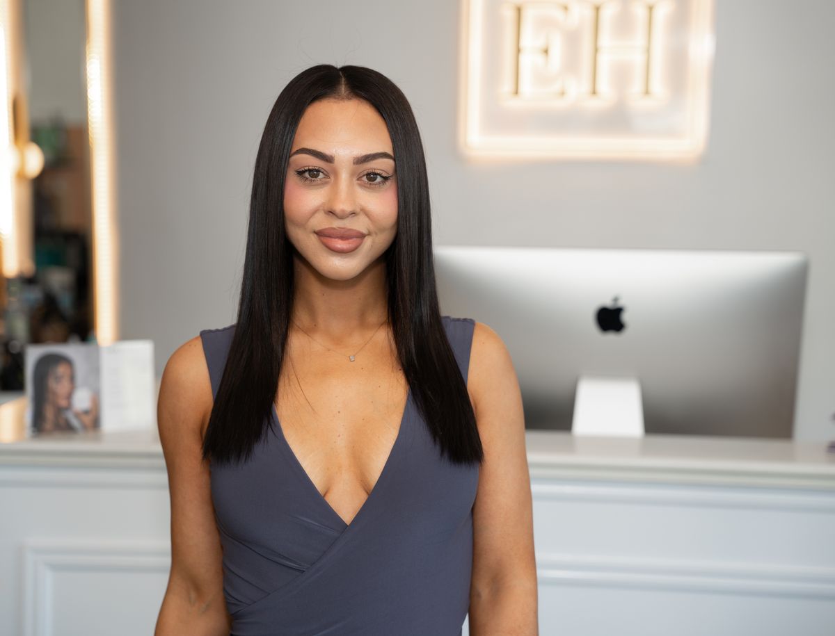 Emilee Hembrow with long straight dark hair standing in an EH salon before her Signature Weft application