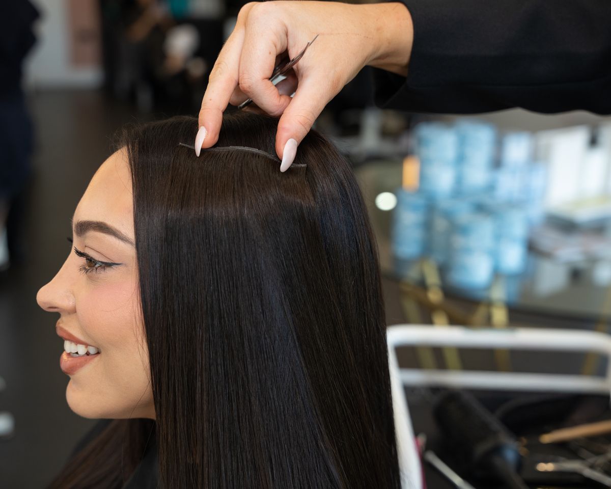 Emilee Hembrow smiling in a salon cape while a Signature Weft row is fitted to her dark hair